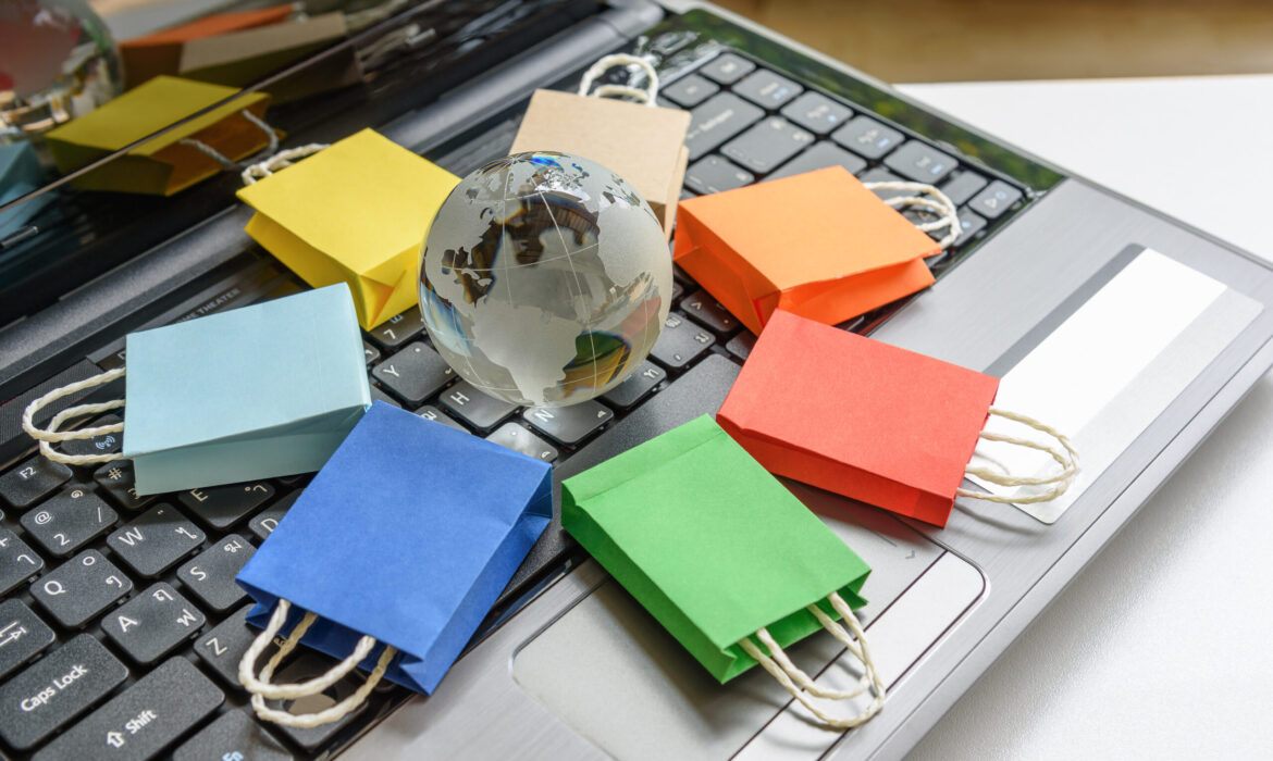 Various shopping bags surrounding a globe on a desk with a laptop