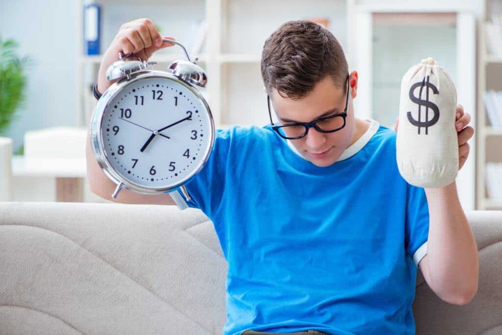 A young person looking busy and holding up a large clock with one hand and money in the other.