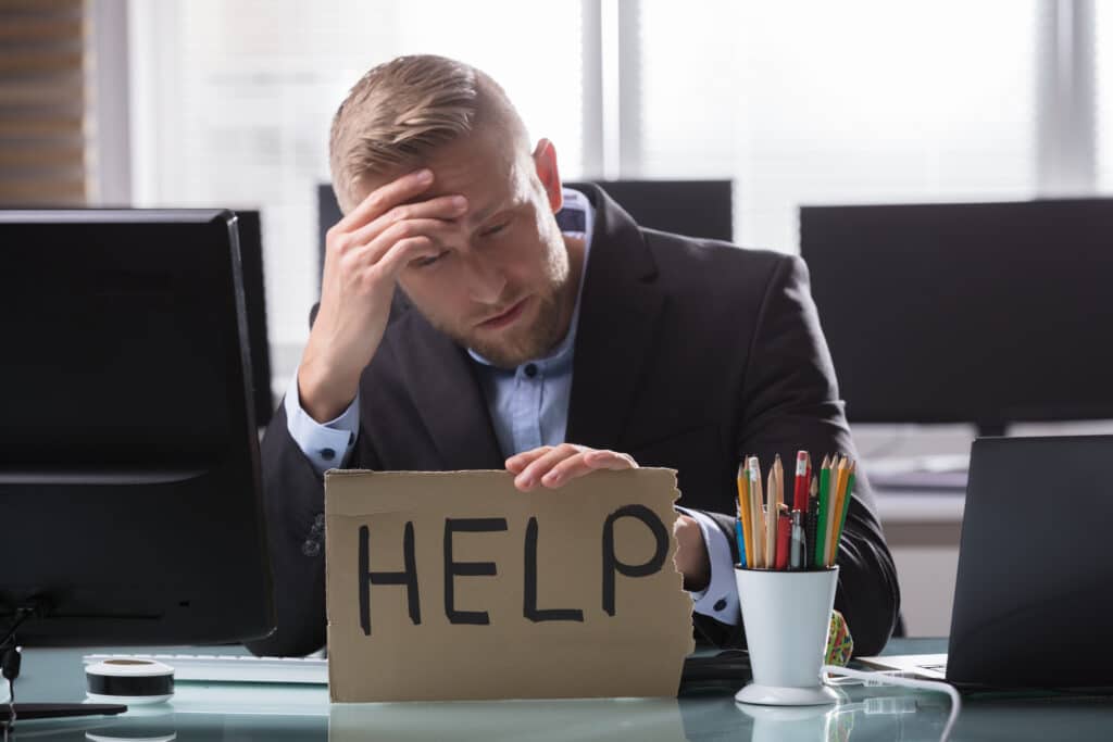 A business man at his desk with a sign asking for help