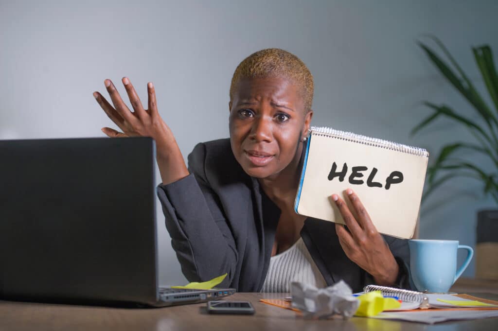 Afircan-American woman at desk with computer and sign with "Help" written on it.